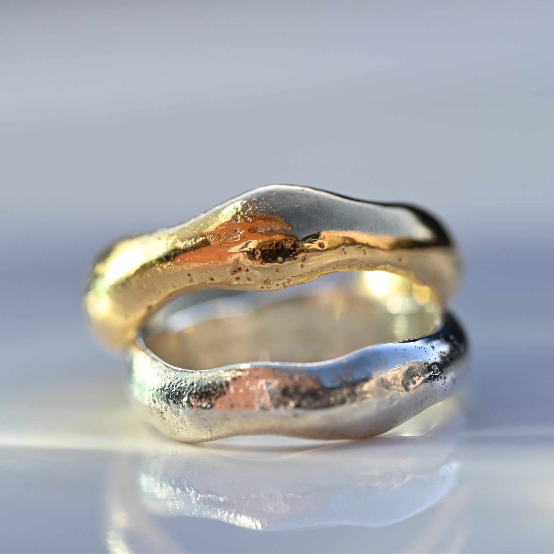 Two textured, organic-shaped rings, one in polished gold and one in polished silver.