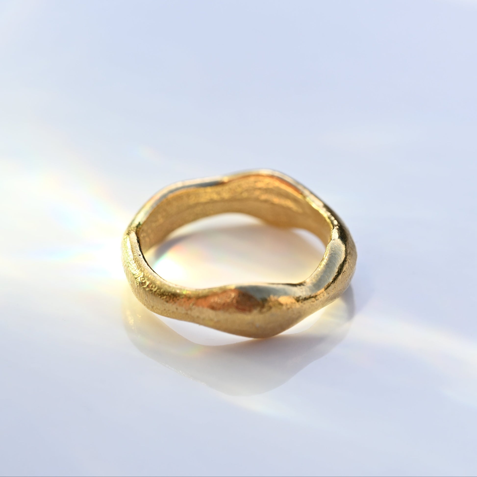 A textured, organic-shaped gold ring with a textured finish, resting on a clean white surface.