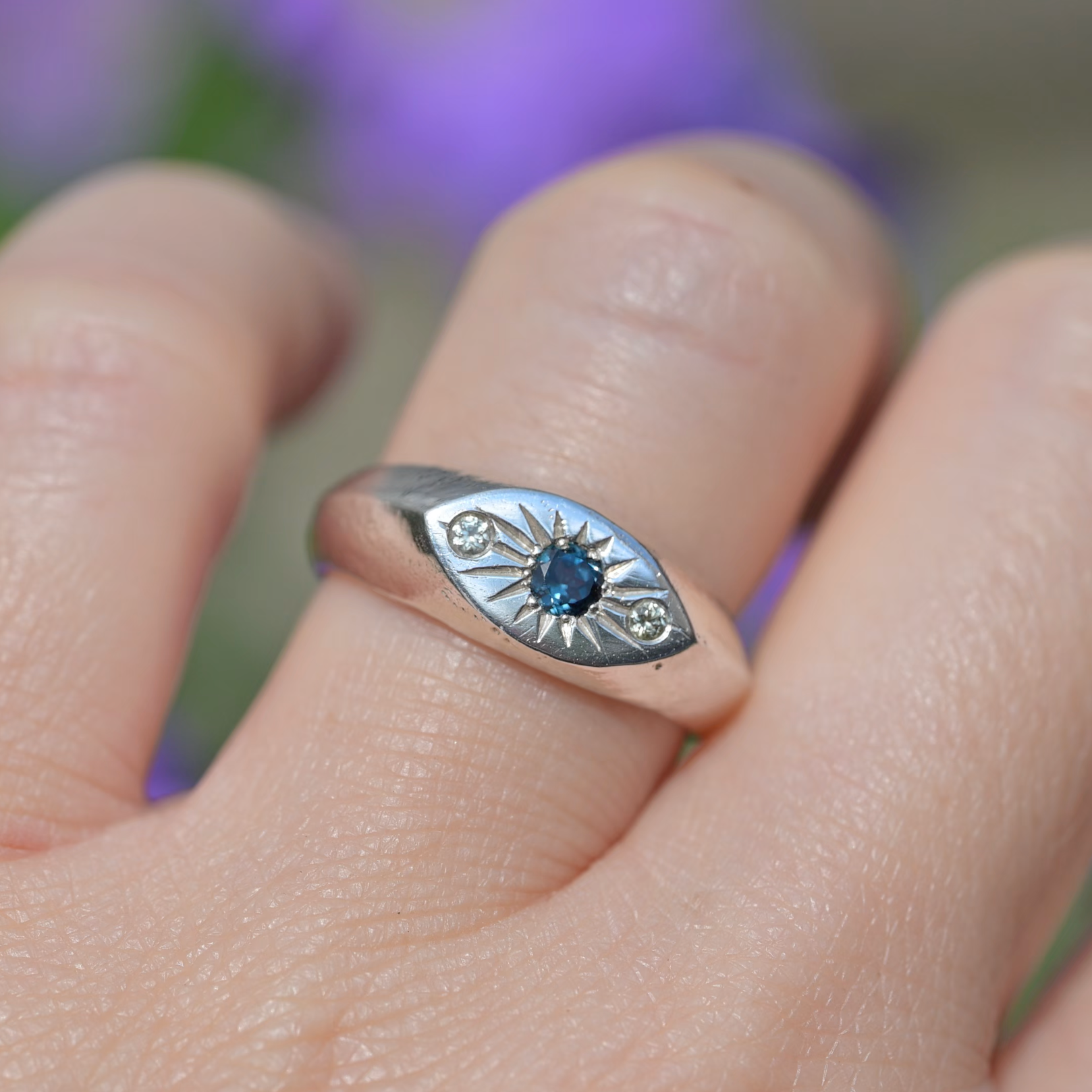 A sterling silver eye ring with a central blue gemstone and small side stones, worn on a person's finger.