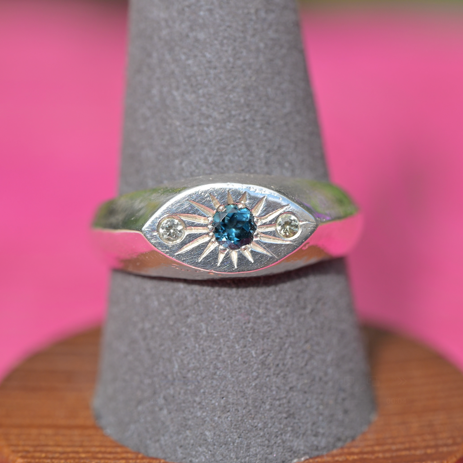 A sterling silver eye-of-providence ring with a central blue gemstone and two small side stones, displayed on a gray ring cone.